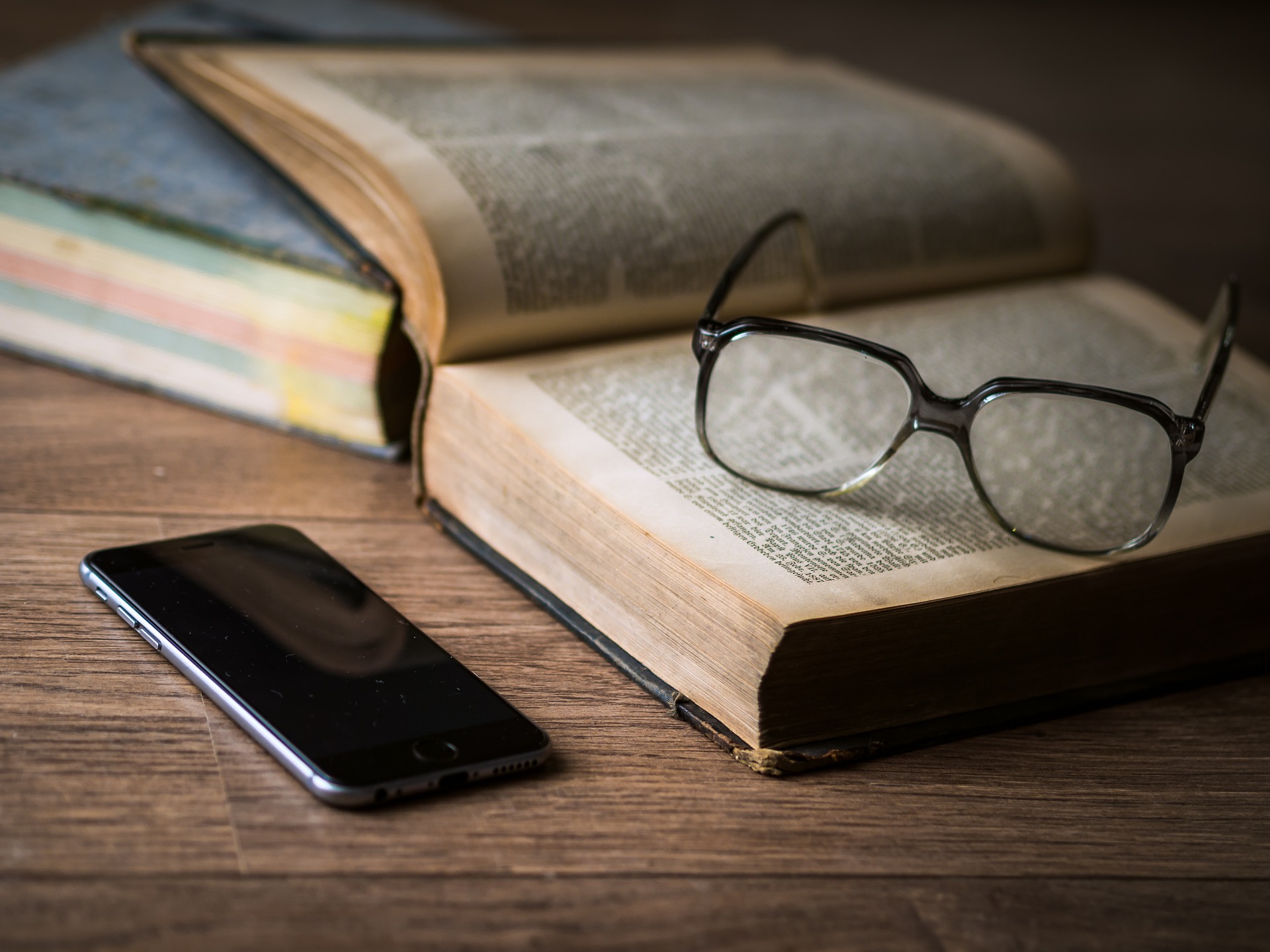 libro con appoggiati occhiali da vista e smartphone sul tavolo
