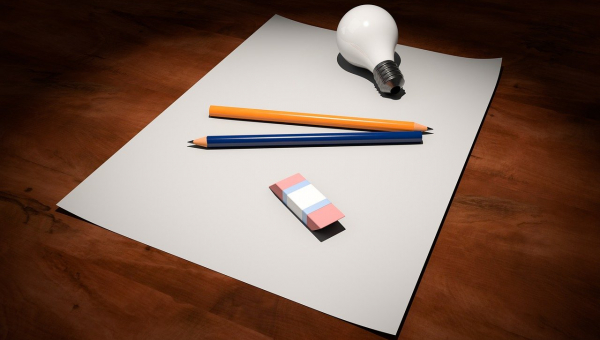 Foglio banco su scrivania di legno con matite, gomma e lampadina creativa